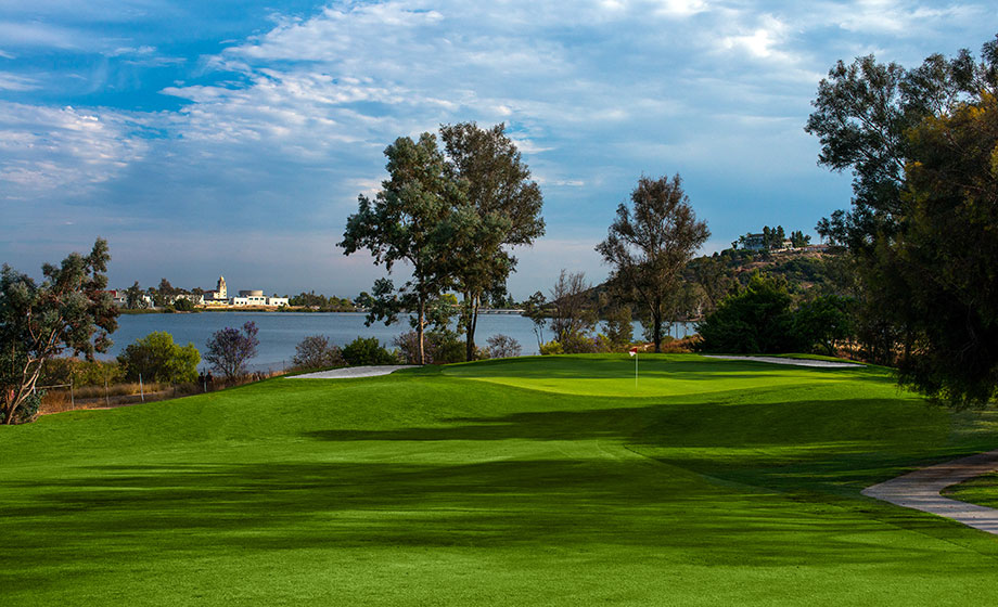 Green golfcourse with tree shadows overlooking body of water midday